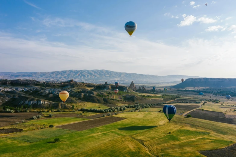 a group of hot air balloons flying over a green field, by Daren Bader, pexels contest winner, ancient marble city, georgic, helicopter view, conde nast traveler photo