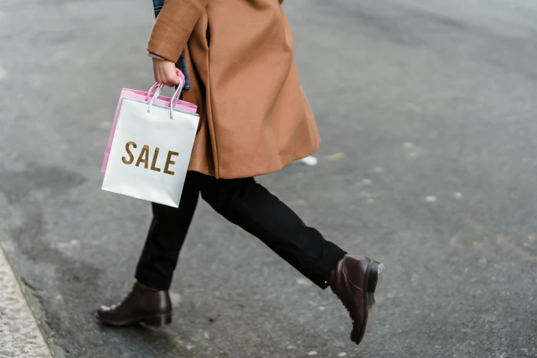 a woman walking down the street carrying shopping bags, pexels contest winner, brown jacket, shows a leg, limited time offer, gold