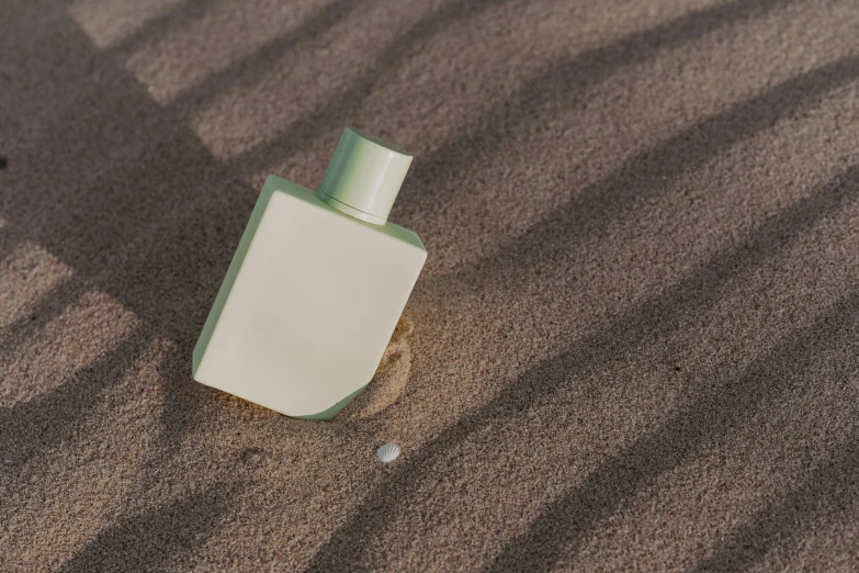 a bottle of lotion sitting in the sand, inspired by Elsa Bleda, unsplash contest winner, conceptual art, burberry, rectangle, greenish skin, handsome