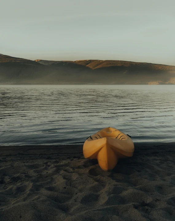 a yellow boat sitting on top of a sandy beach, a picture, by Jessie Algie, unsplash contest winner, on the calm lake, iceland hills in the background, faded glow, paddle of water