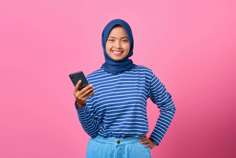 a woman in a blue and white striped shirt holding a cell phone, inspired by JoWOnder, shutterstock, hurufiyya, ((pink)), ismail, frontal pose, outfit photograph