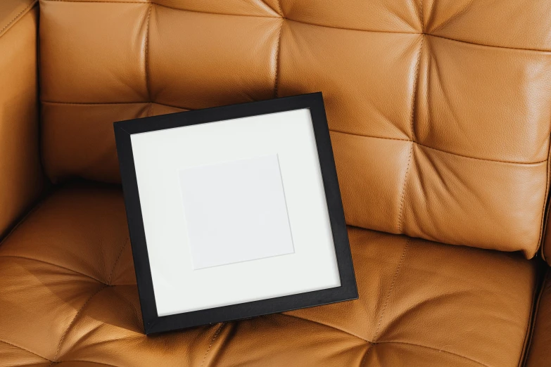 a picture frame sitting on top of a brown leather chair, inspired by Robert Mapplethorpe, pexels contest winner, squares, detailed product image, square facial structure, plush leather pad