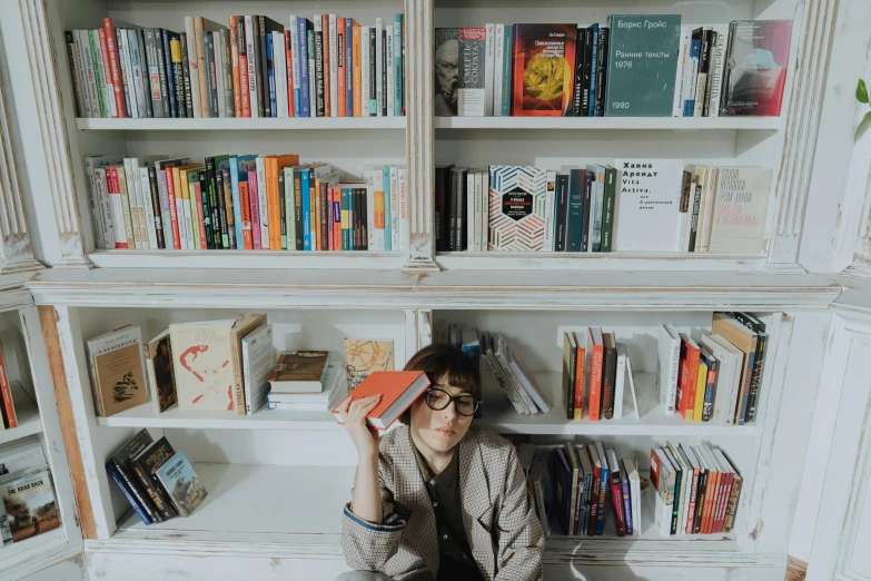 a woman sitting on a chair in front of a bookshelf, pexels contest winner, rebecca sugar, library nerd glasses, flatlay book collection, androgynous person