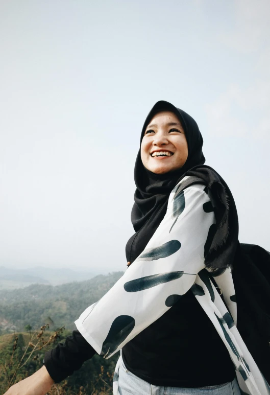 a woman standing on top of a hill, inspired by JoWOnder, pexels contest winner, sumatraism, wrapped in a black scarf, mutahar laughing, black on white, batik