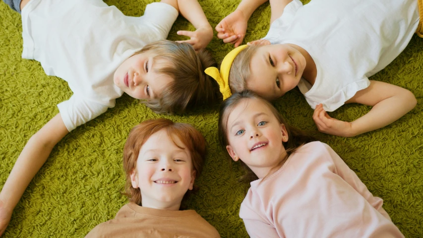 a group of children laying on top of a green carpet, high forehead, caring fatherly wide forehead, rugs, thumbnail