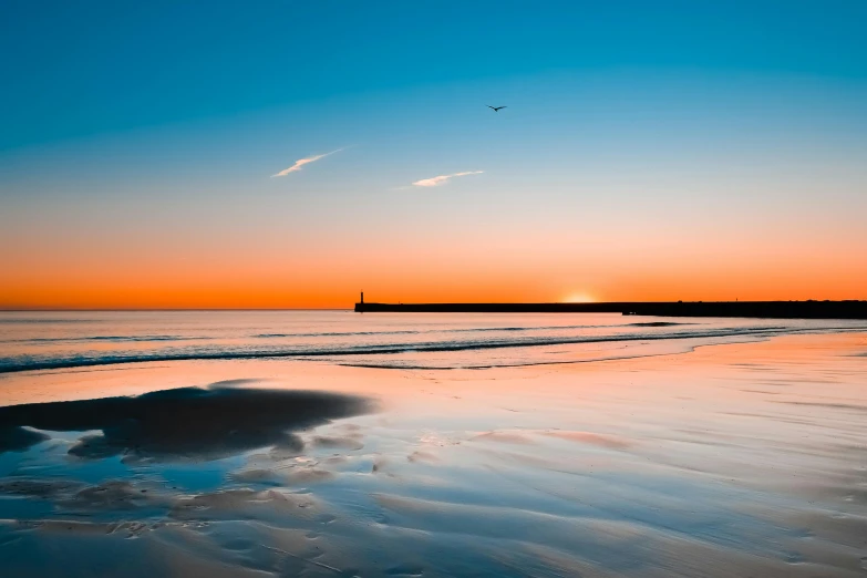 a large body of water sitting on top of a sandy beach, by Eglon van der Neer, pexels contest winner, sunrise colors, birds flying in the distance, bold lighthouse in horizon, smooth reflections