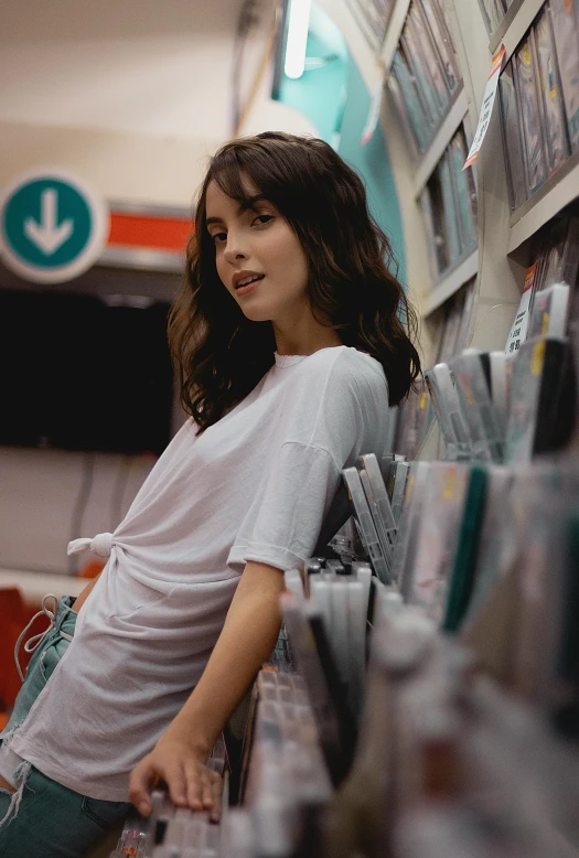 a woman leaning against a wall in a store, an album cover, inspired by Elsa Bleda, pexels contest winner, happening, dressed in a white t-shirt, at target, 2 4 year old female model, vhs style
