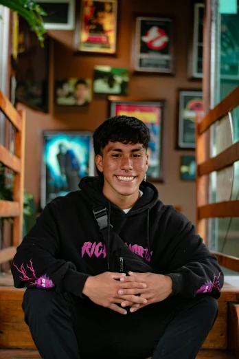a young man sitting on the steps of a building, a portrait, by Robbie Trevino, sitting on a store shelf, wearing a pink hoodie, happily smiling at the camera, joseph moncada