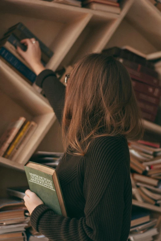 a woman standing in front of a bookshelf holding a book, pexels contest winner, girl with brown hair, up there, hazy, gif