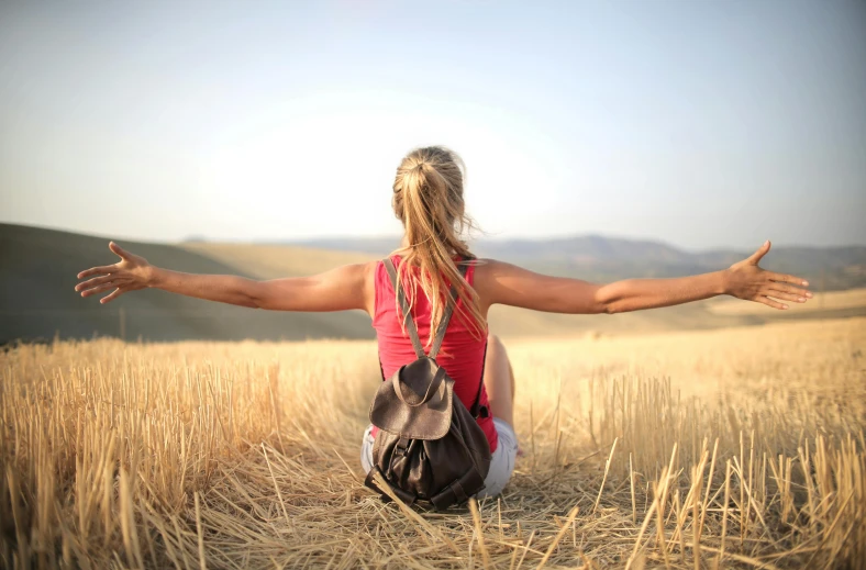 a woman sitting in a field with her arms outstretched, pexels contest winner, arms behind back, traveller, health supporter, looking across the shoulder