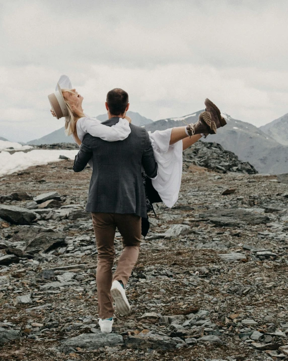 a man carrying a woman up in the air on top of a mountain, by Lee Loughridge, pexels contest winner, elegantly dressed, walking away, rugged details, wedding