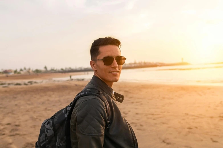 a man standing on top of a sandy beach, wearing shades, an epic non - binary model, a man wearing a backpack, profile image