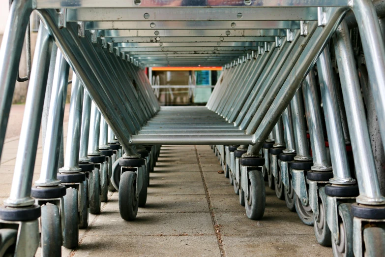 a row of shopping carts sitting on top of a sidewalk, in a warehouse, profile image, head down, grey