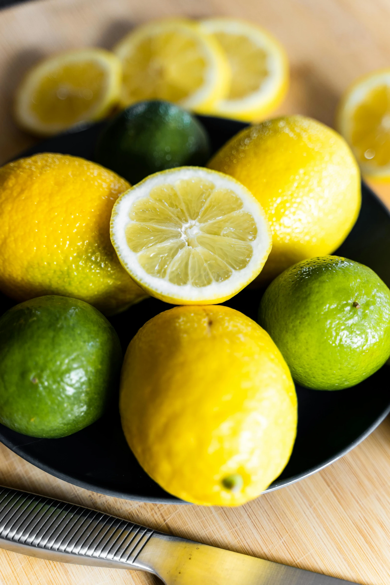 a plate of lemons and limes on a table, piled around, close together, bowl of fruit, upclose
