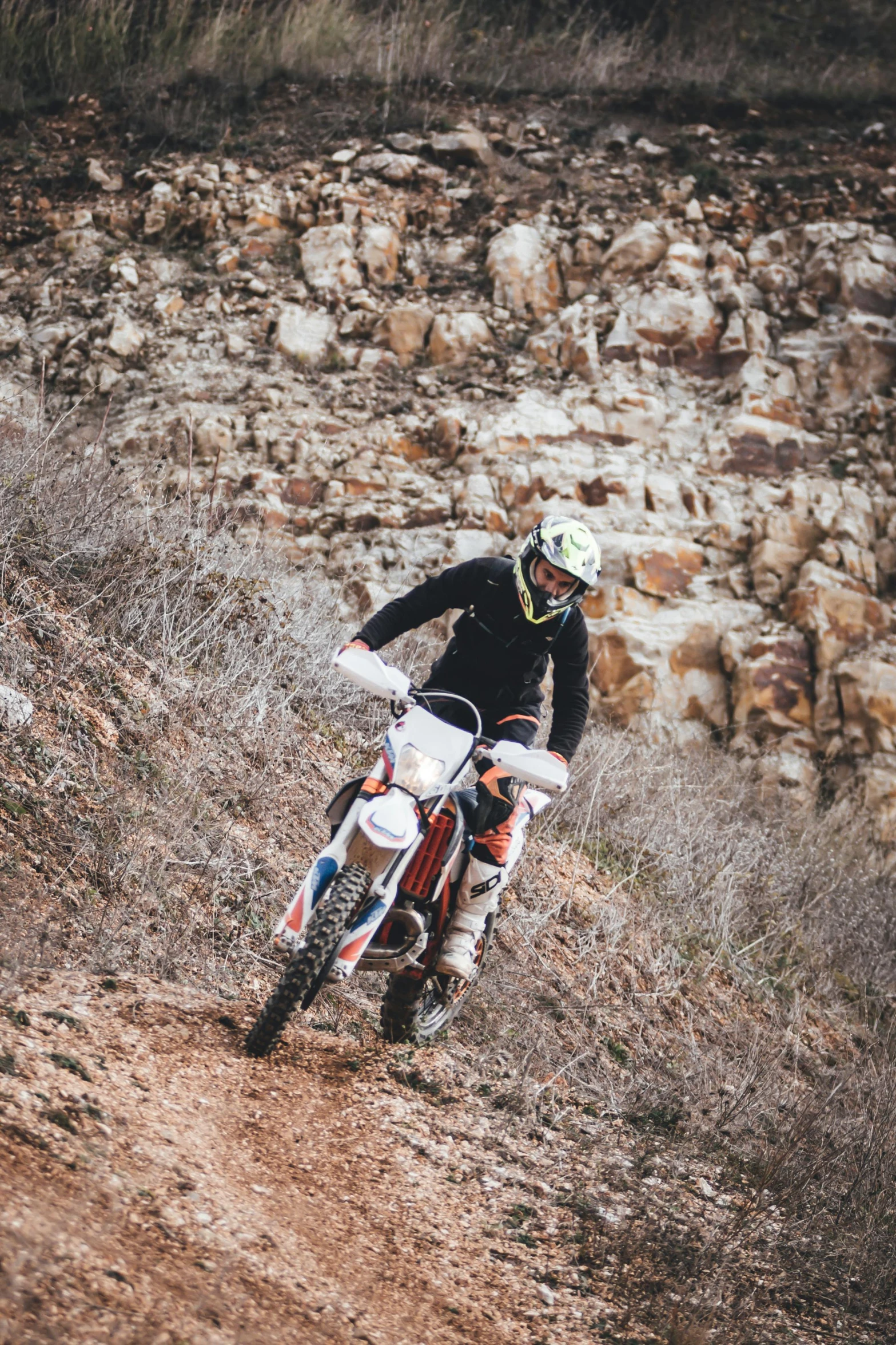 a man riding a dirt bike down a hill, a picture, unsplash, figuration libre, 2 5 6 x 2 5 6 pixels, white and red body armor, rocky cliff, oman