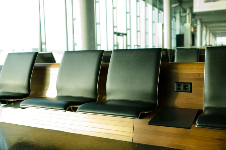 a row of black leather chairs sitting next to each other, by Thomas Häfner, unsplash, black. airports, wooden banks, iceland, thumbnail