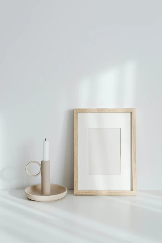 a picture frame sitting on a shelf next to a candle, a minimalist painting, minimalism, light wood, set against a white background, jovana rikalo, cream paper