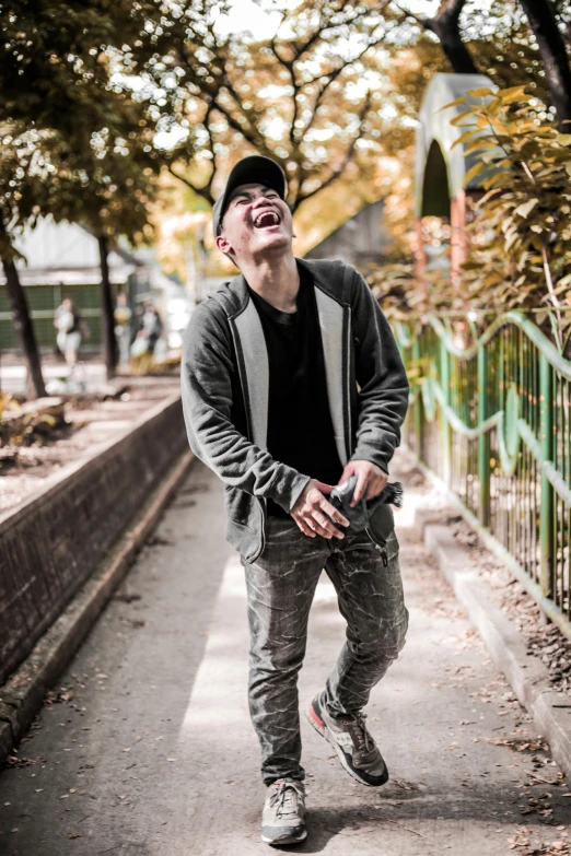 a man standing on a sidewalk next to a fence, pexels contest winner, laughter and screaming face, wearing jeans and a black hoodie, jesper esjing, avatar image