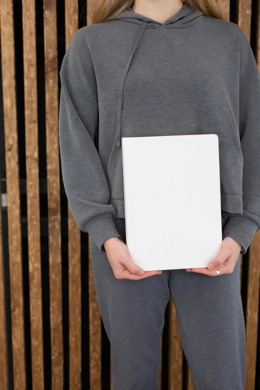 a woman standing in front of a wooden wall holding a white box, a picture, unsplash, he is holding a large book, wearing a tracksuit, high resolution photo, no - text no - logo