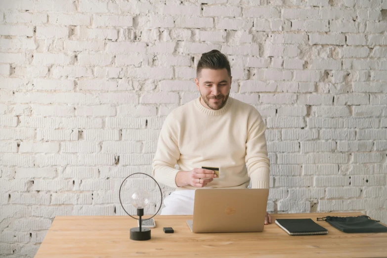 a man sitting at a table with a laptop and a credit card, pexels contest winner, wearing a white sweater, avatar image, man standing, with a small beard