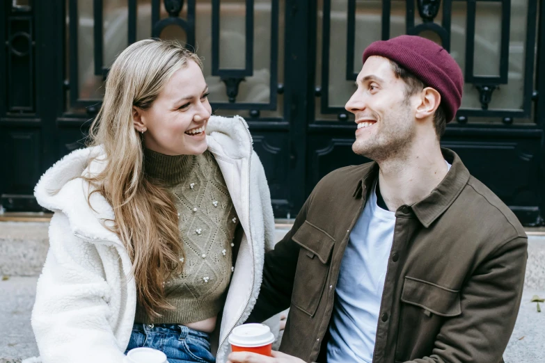 a man and a woman sitting next to each other, trending on pexels, happening, flirting smiling, background image, britt marling style 3/4, in city street