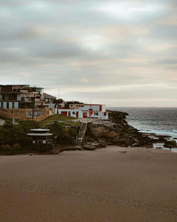 a man flying a kite on top of a sandy beach, by Elsa Bleda, pexels contest winner, waterfront houses, rocky coast, gif, slight overcast lighting