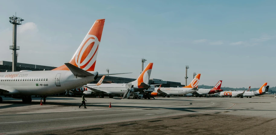 a large jetliner sitting on top of an airport tarmac, by Daniel Lieske, pexels contest winner, incoherents, orange and white, in a row, são paulo, avatar image