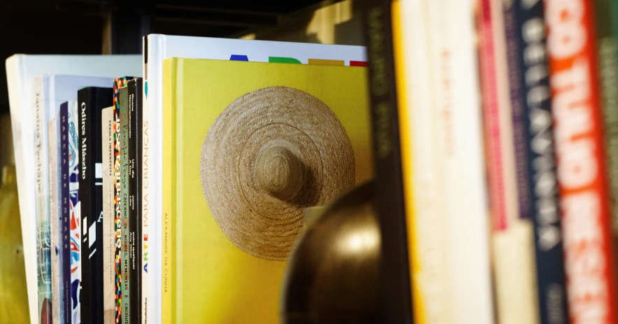 a book shelf filled with books and a hat on top of it, an album cover, inspired by Germán Londoño, unsplash, figuration libre, glossy yellow, organic detail, hay, close-up shot taken from behind