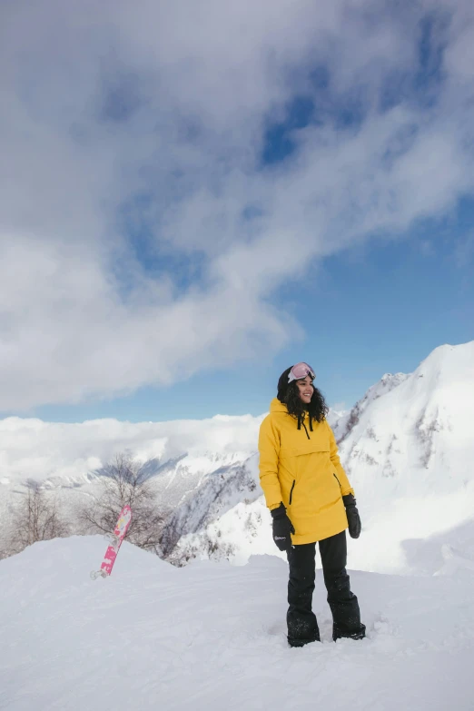 a woman standing on top of a snow covered mountain, wearing a yellow hoodie, new zeeland, psychedelic ski resort, profile image