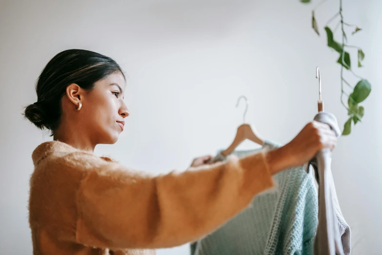 a woman hanging a sweater on a hanger, trending on pexels, looking to the right, performing, profile image, presenting wares