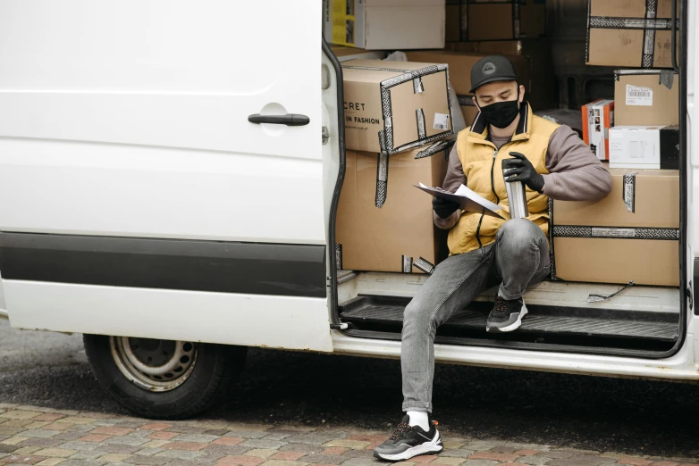 a man that is sitting in the back of a van, cardboard, wearing facemask, ecommerce photograph, illustration »