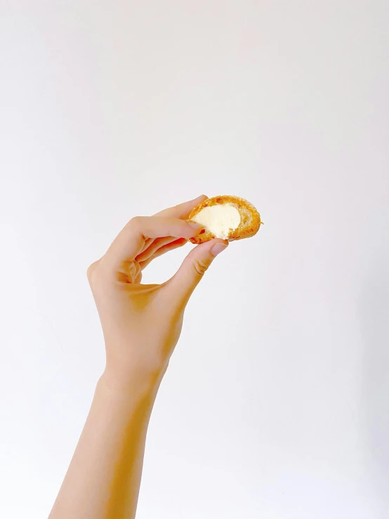 a close up of a person holding a piece of food, by David Diao, minimalism, cream, cheesy, extra crisp image, bakery