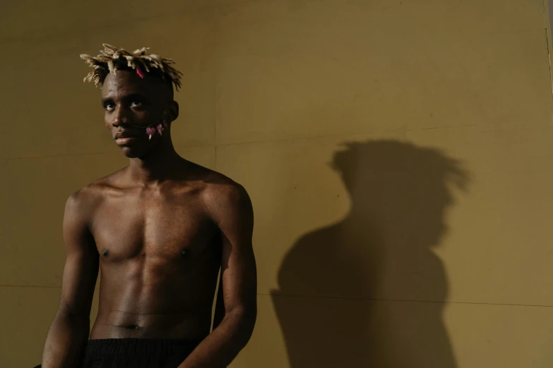 a man standing in front of a yellow wall, by Chinwe Chukwuogo-Roy, visual art, extremely pale blond hair, loincloth, xxxtentacion, in a black room