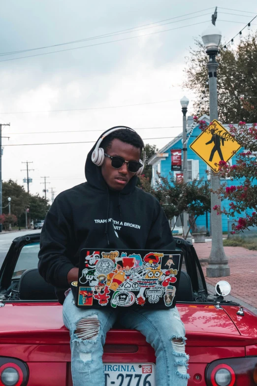 a man sitting on top of a red car, an album cover, trending on pexels, graffiti, sitting at a computer, black teenage boy, silly and serious, black hoodie techie
