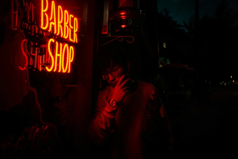 a man standing in front of a barber shop, inspired by Elsa Bleda, pexels contest winner, red neon, smoker, busy night, glow in the dark