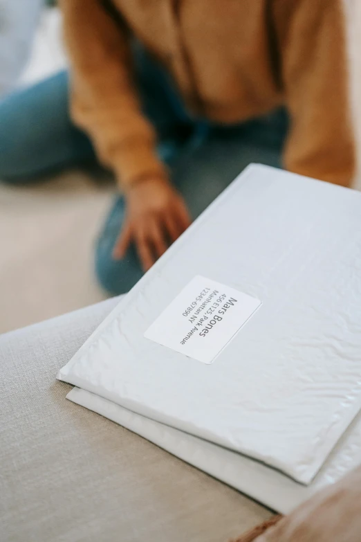 a woman sitting on top of a bed next to a pile of paper, private press, product label, on a couch, opening shot, detailed product image