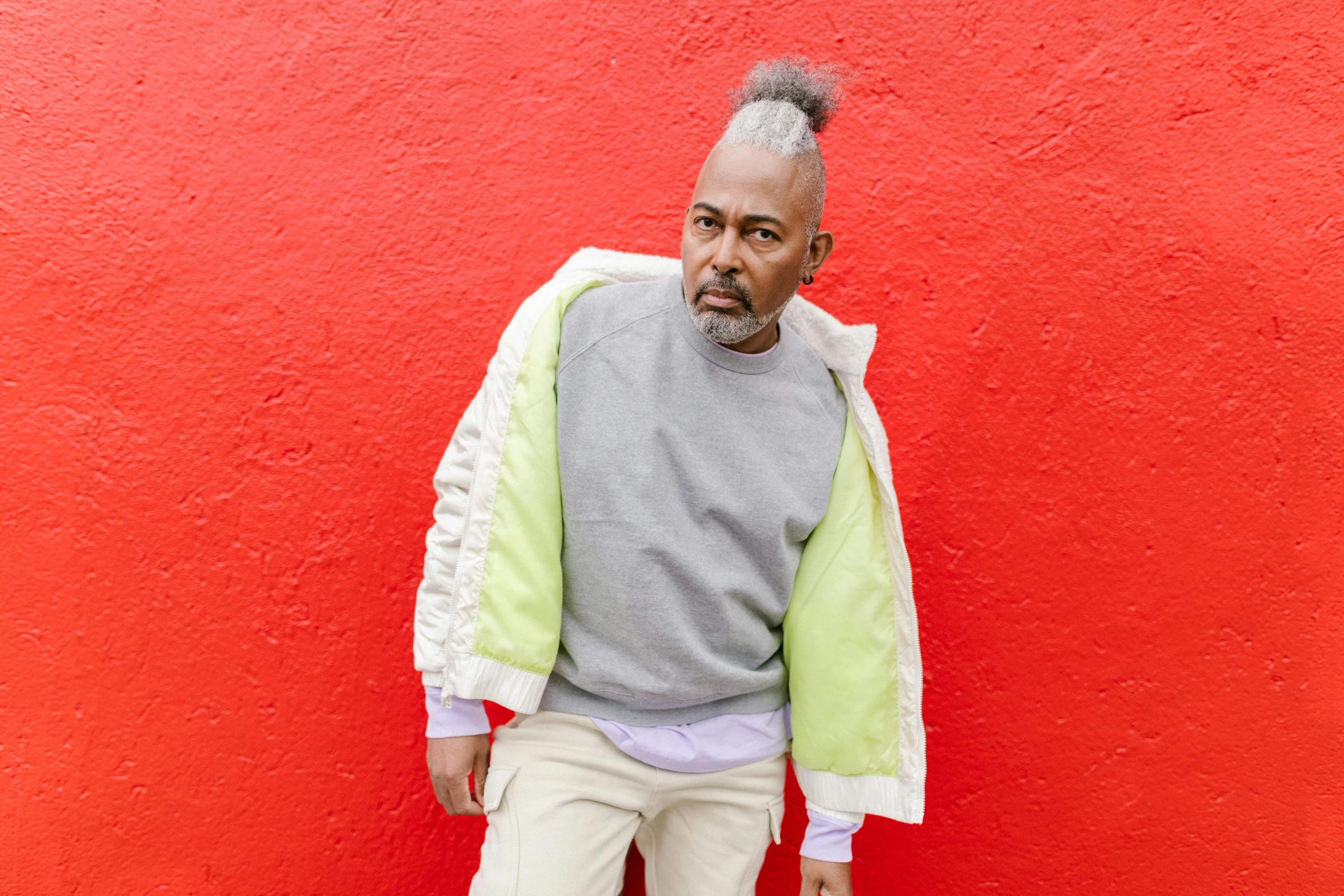 a man standing in front of a red wall, by Winona Nelson, grey skinned, wearing a sweater, with a mohawk, in front of white back drop