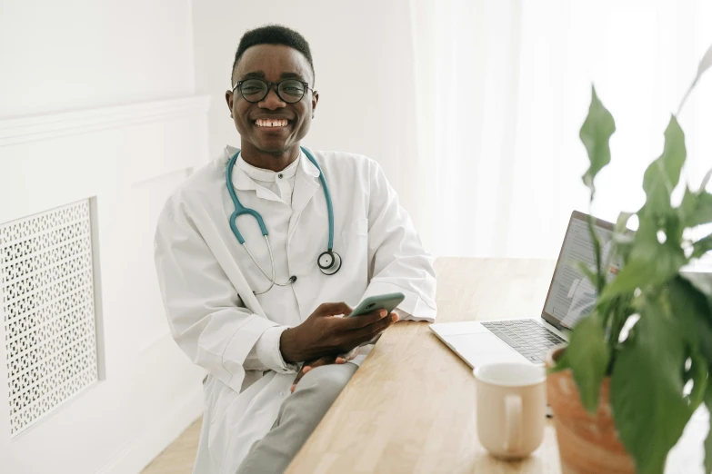 a man with a stethoscope sitting in front of a laptop, a photo, inspired by Dr. Atl, pexels, happening, brown skin man with a giant grin, holding a very advance phone, sitting on top a table, thumbnail