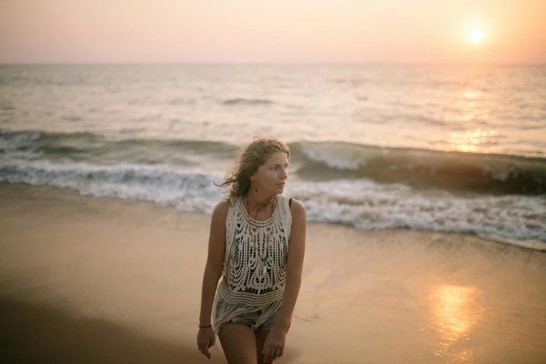 a woman standing on top of a beach next to the ocean, a portrait, unsplash, soft warm light, sleeveless, singer songwriter, extremely intricate