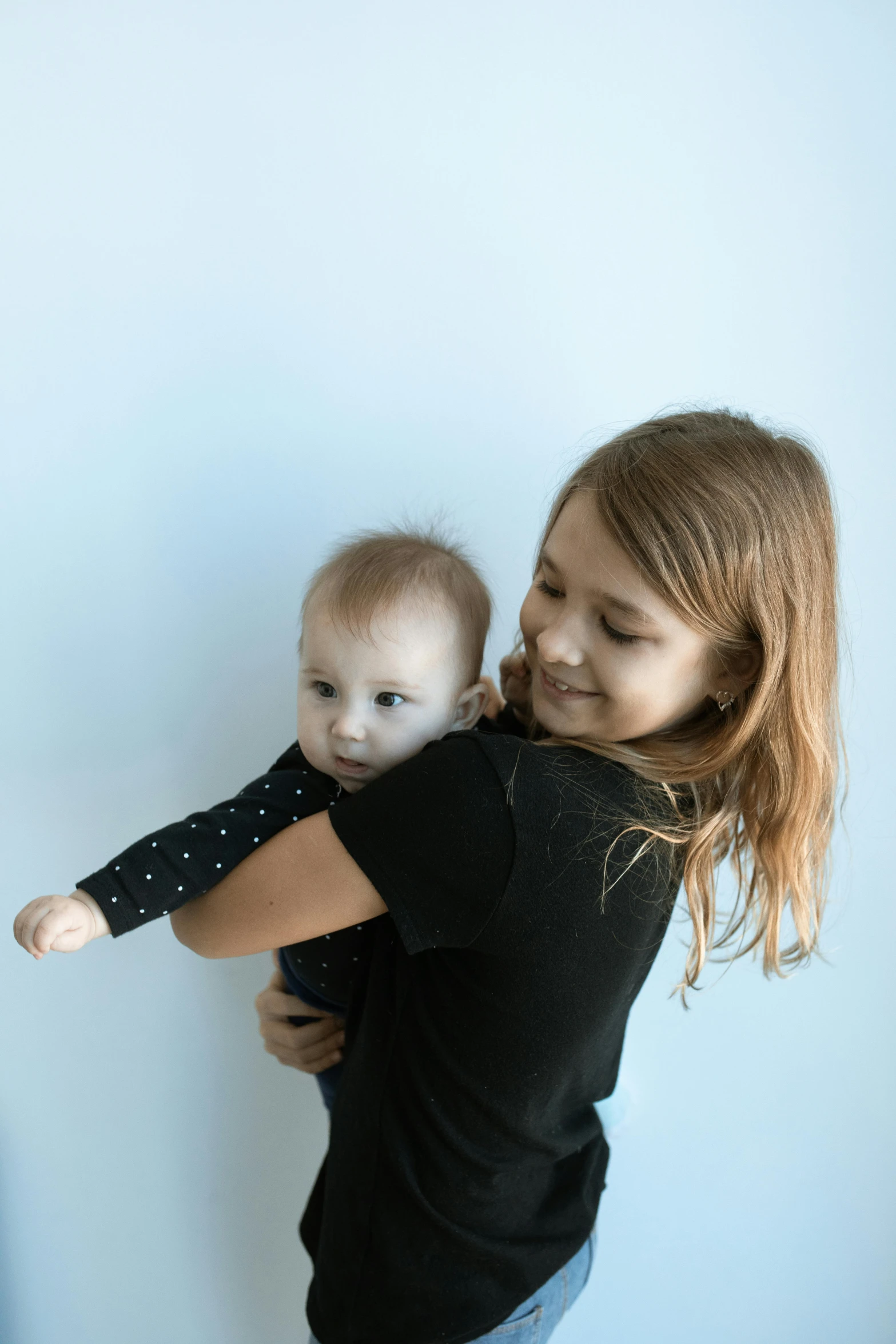 a woman holding a baby in her arms, unsplash, antipodeans, plain background, siblings, softplay, portrait image