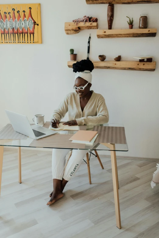 a woman sitting at a table working on a laptop, by Arabella Rankin, trending on pexels, afrofuturism, in a white boho style studio, sitting on a mocha-colored table, full body hero, professional image