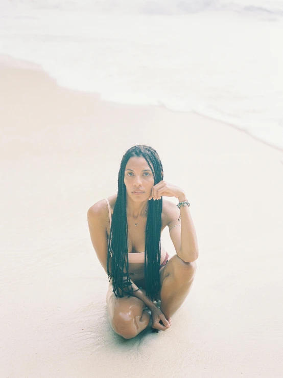 a woman sitting on top of a beach next to the ocean, box braids, wet skin, bella poarch, standing in sand