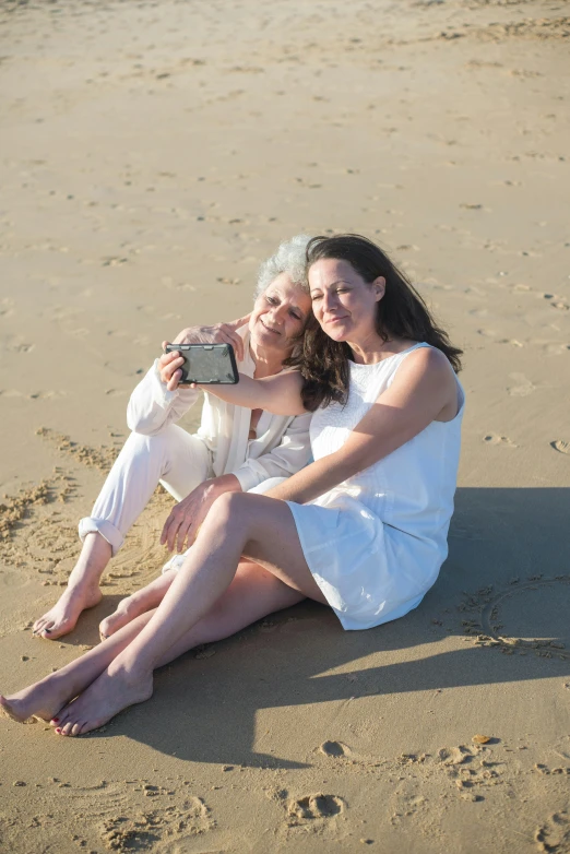 a couple of women sitting on top of a sandy beach, taking a picture, family photo, bright white light, older woman