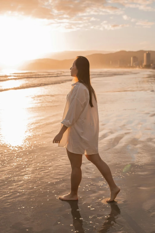 a woman walking on the beach at sunset, inspired by Sun Long, pexels contest winner, renaissance, wearing a linen shirt, gold coast australia, brunette, young woman