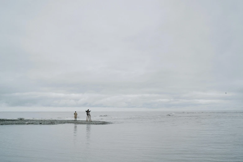 a couple of people that are standing in the water, unsplash, minimalism, overcast gray skies, haida, ignant, hunting