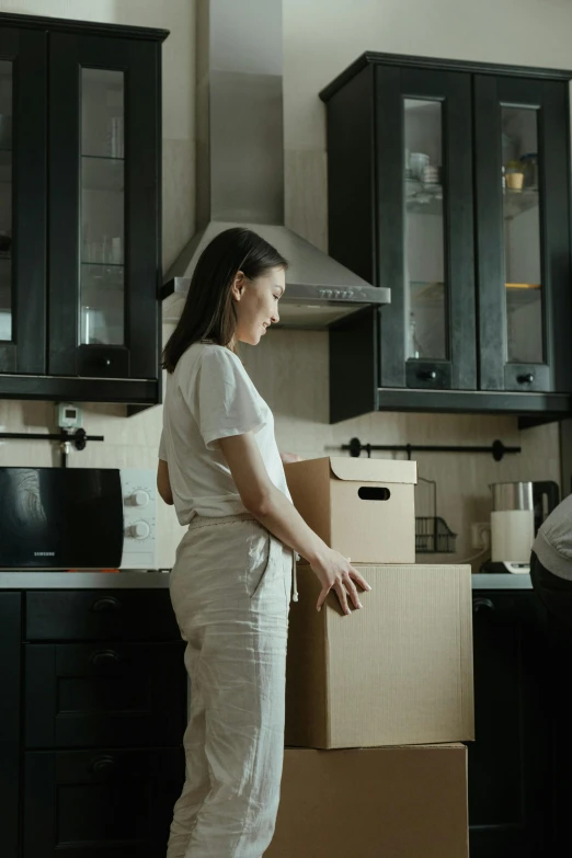 a woman standing in a kitchen next to a stack of boxes, pexels contest winner, medium shot of two characters, reuniting, australian, low quality photo