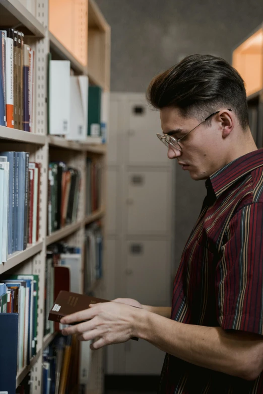 a man looking at a book in a library, pexels contest winner, non binary model, thin young male, gif, man standing