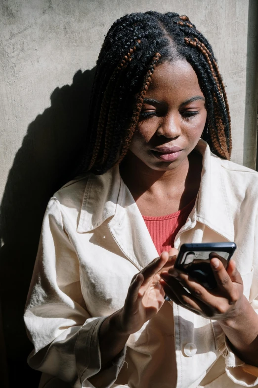 a woman is looking at her cell phone, by Matija Jama, trending on pexels, light skinned african young girl, subtle shadows, woman with braided brown hair, 2040