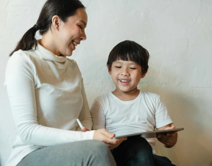 a woman sitting next to a child on a couch, a child's drawing, pexels contest winner, mingei, earing a shirt laughing, writing on a clipboard, asian male, teacher