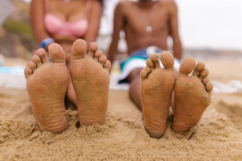 a couple of women sitting on top of a sandy beach, trending on pexels, renaissance, realistic human feet, with brown skin, big foot, laying down